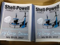 Two stacks of spiral-bound booklets titled "Shell-Powell Family Reunion" are displayed, with details of the event held in Hot Springs, Arkansas from July 20-23, 2017. The cover features an illustration of a fountain.