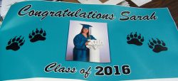 A graduation banner with "Congratulations Sarah" and "Class of 2016" text, featuring a photo of a graduate in cap and gown, and decorated with paw prints.