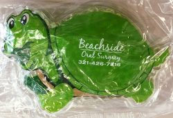 A turtle-shaped ice pack with "Beachside Oral Surgery" and the phone number 321-426-7816 printed on the shell.