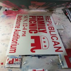 A sign printed with "Republican Family Picnic, Sun 12-4 PM, Melbourne Auditorium" in red and white on a corrugated board.