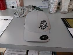 A gray cap with a "Brevard Patriot" logo sits on a desk surrounded by various papers, a plastic cup, and a piece of fabric.